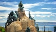 Escultura de personas sobre rocas con vista al mar.