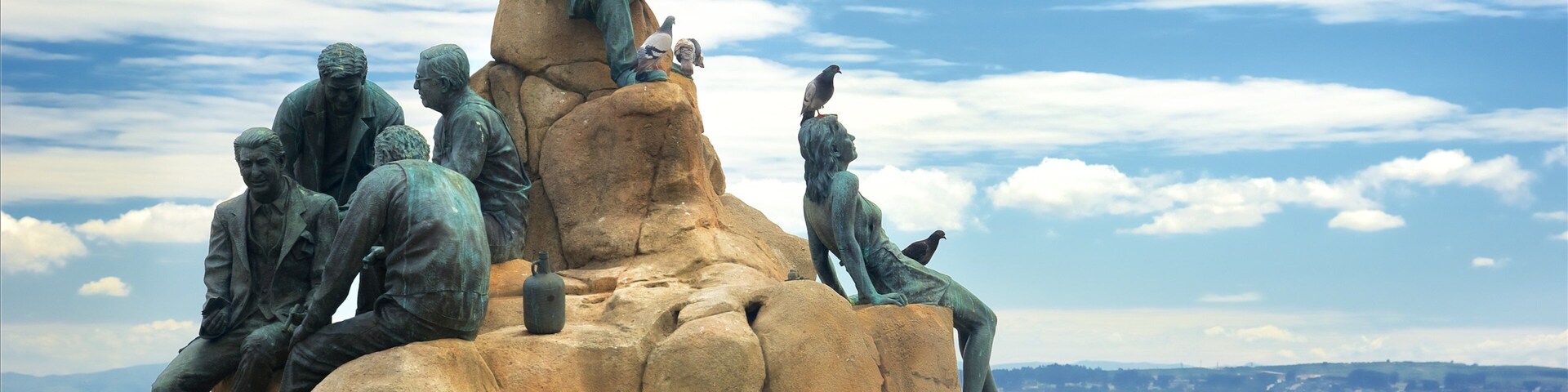 Escultura de pessoas sobre rochas, com vista para o mar.