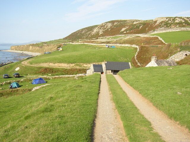 A coastal path with tents, a small building, and a cliffside.
