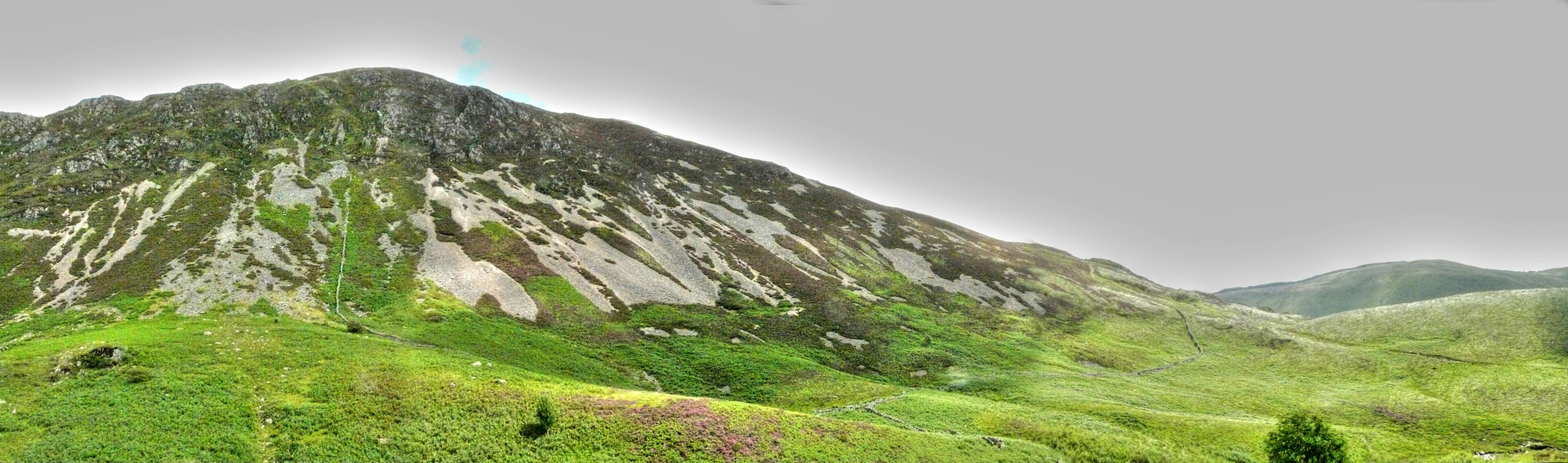 A mountain with a grassy foreground and a cloudy sky.