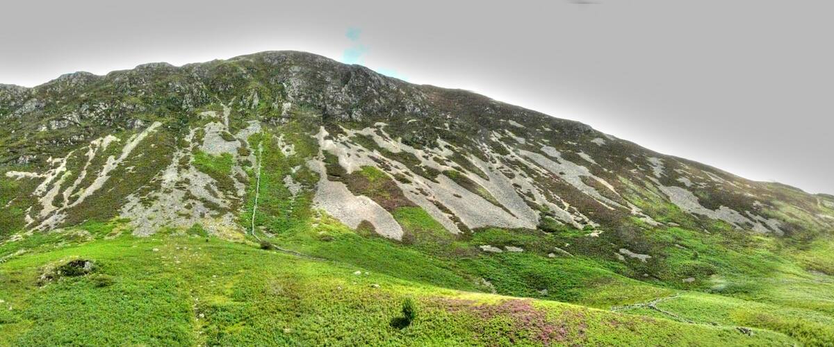 A mountain with a grassy foreground and a cloudy sky.