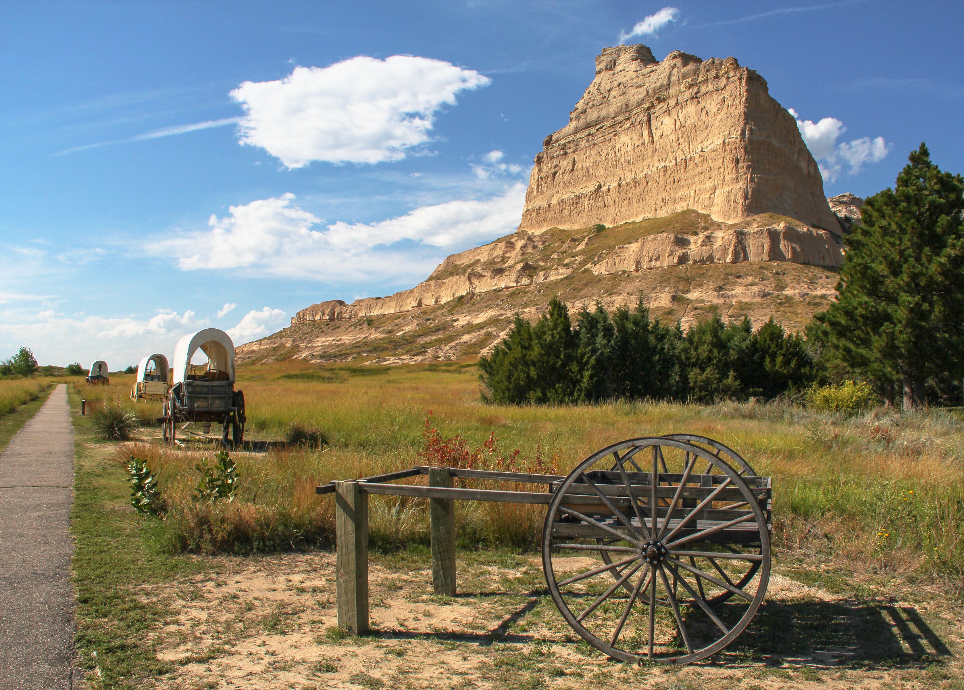 A historical site with a large rock formation, a dirt path, and vintage carriages.