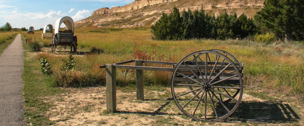 A historical site with a large rock formation, a dirt path, and vintage carriages.