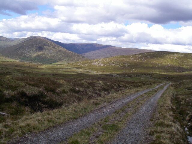 A gravel path in a hilly, grassy landscape with mountains in the background.