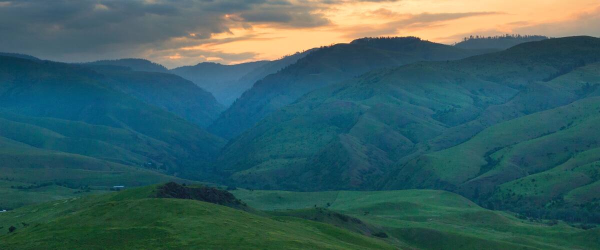 Rolling green hills and a valley under a cloudy sky.