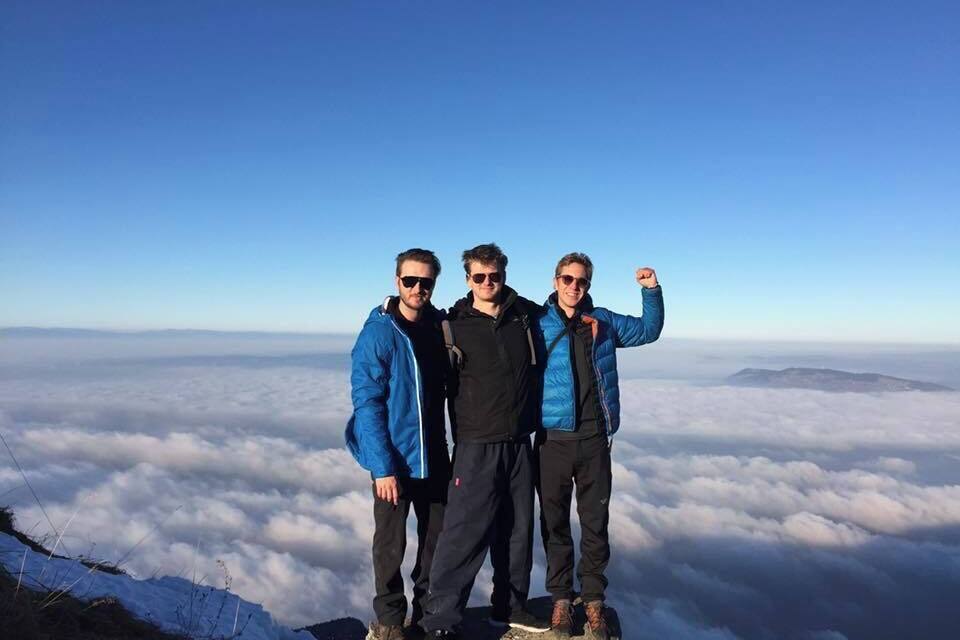 Tres personas en la cima de una montaña, con una vista de nubes abajo.