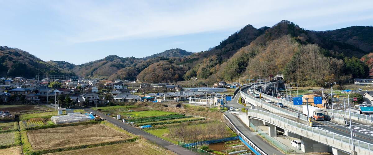 A highway overpass with a mountainous backdrop, fields, and residential areas.