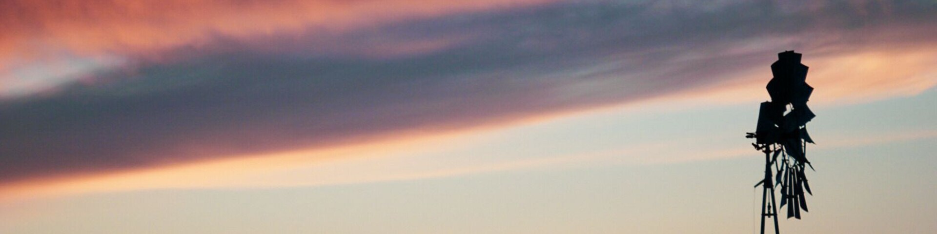 Um moinho de vento silhueta contra um céu vibrante ao pôr do sol.
