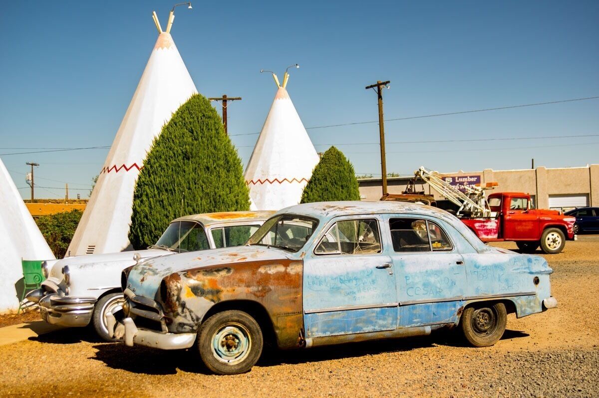 A vintage blue and white car parked in front of white teepees.