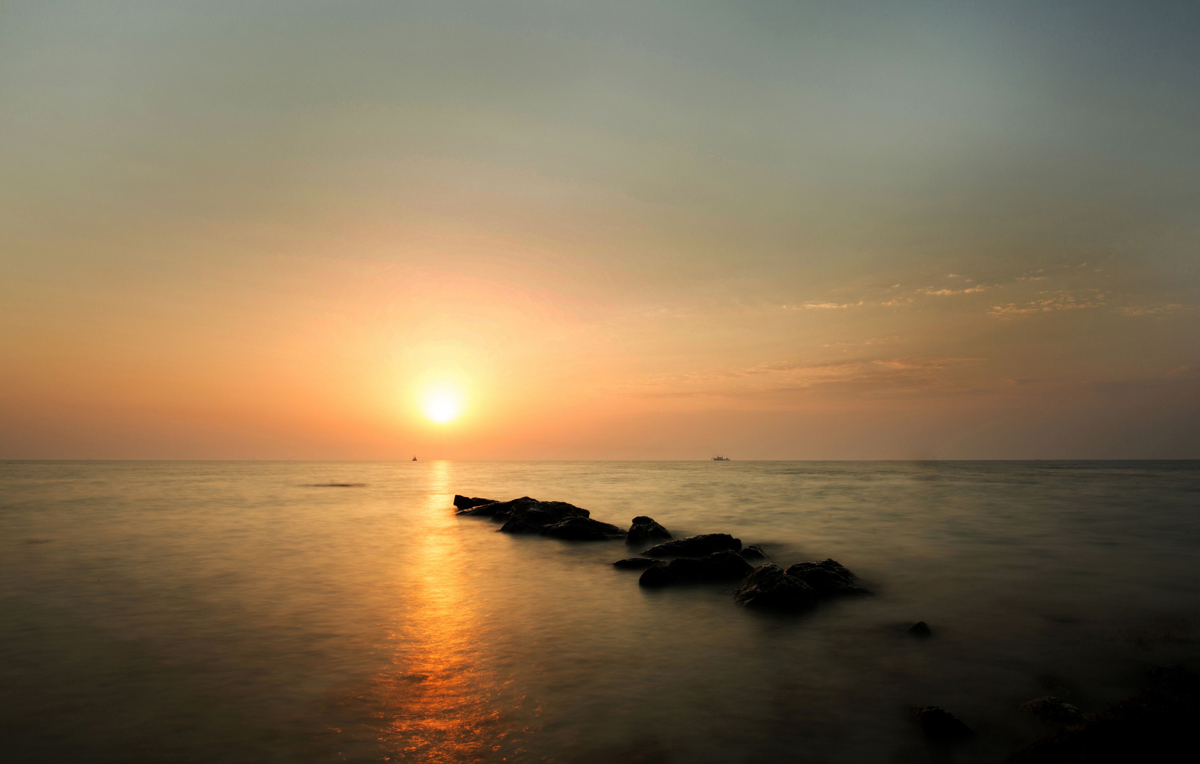 Atardecer sobre aguas oceánicas tranquilas con rocas al frente.