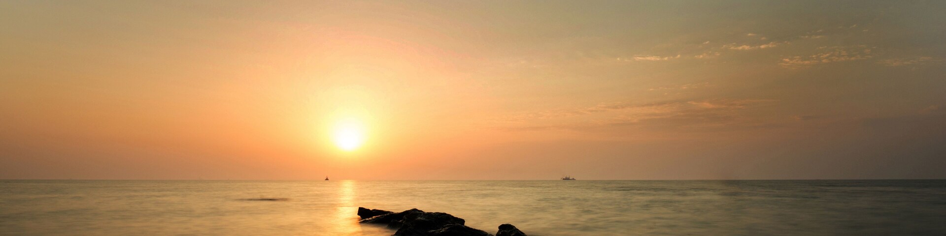 Atardecer sobre aguas oceánicas tranquilas con rocas al frente.