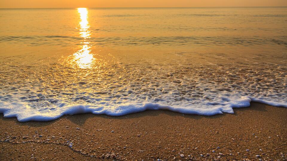 A beach with golden sand and gentle waves at sunset.