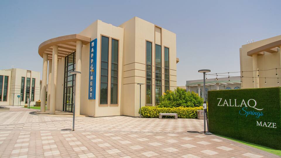 A modern building with a sign reading "HAPINEST" and another sign for "ZALLAQ Springs Maze".