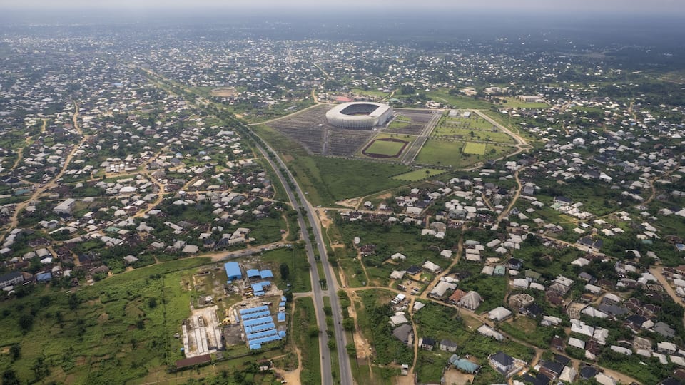 Aerial view of a stadium surrounded by a vast parking area and green spaces blending into the city's edge, Akwa Ibom, Uyo, Nigeria.