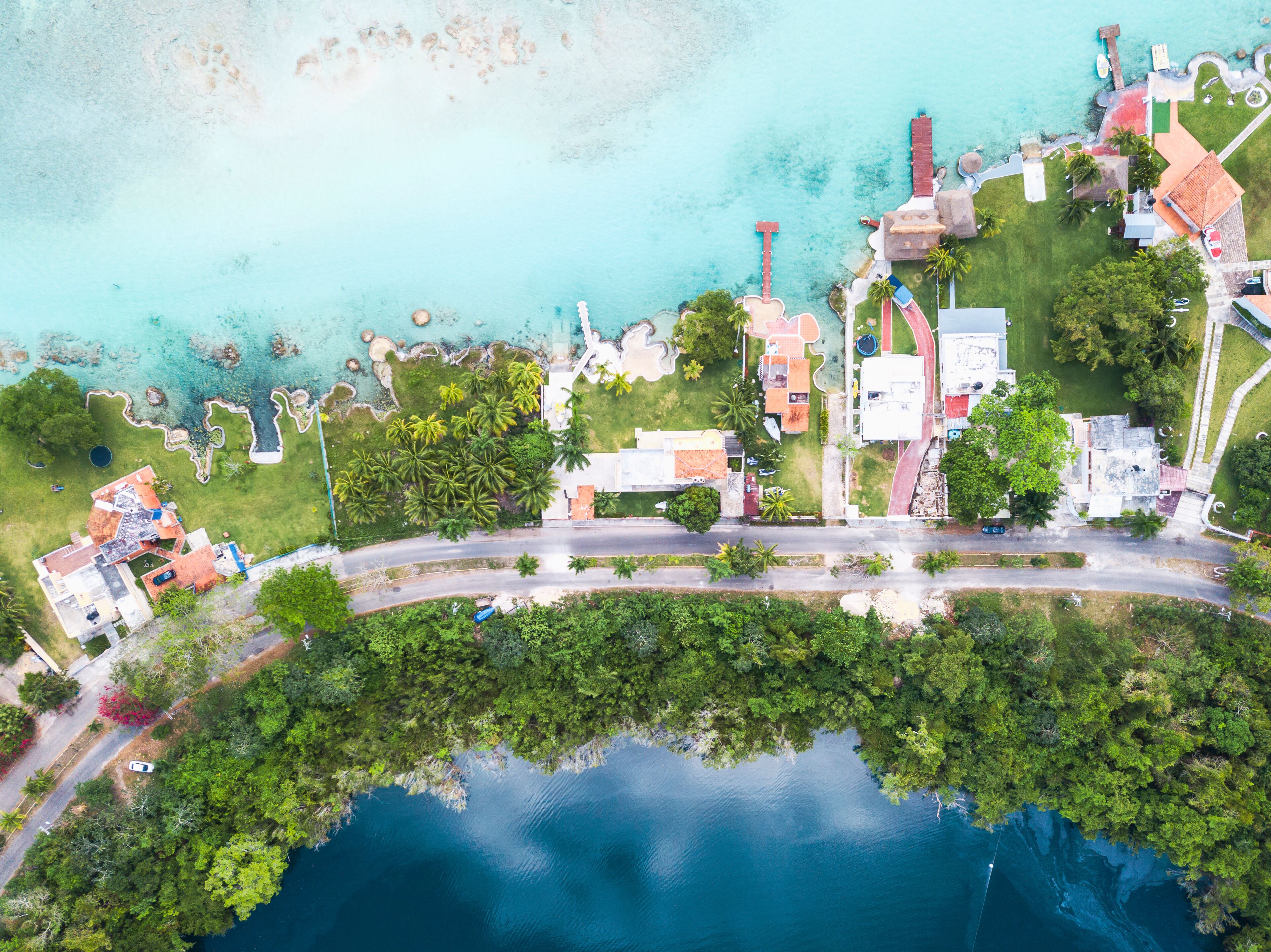 An aerial view of a coastal area with clear turquoise waters, a winding road, and lush greenery.