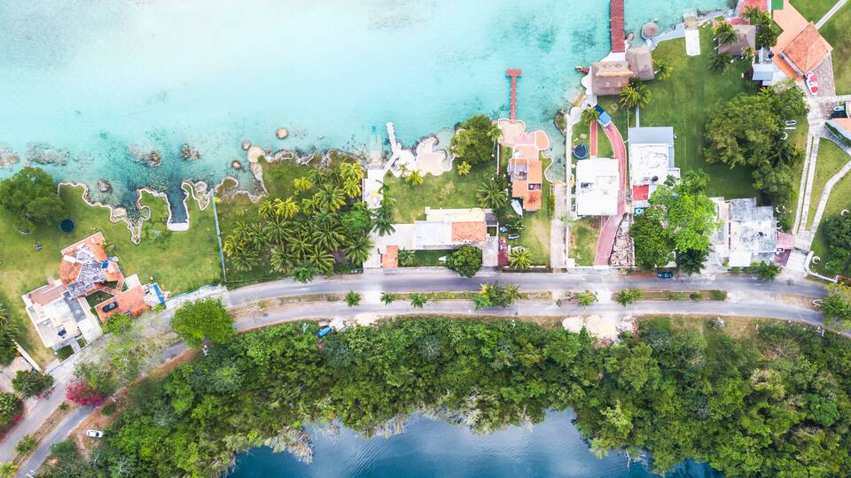 An aerial view of a coastal area with clear turquoise waters, a winding road, and lush greenery.