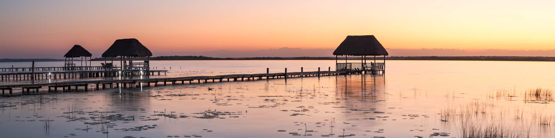 A pier extending into calm waters with thatched-roof structures at the end.