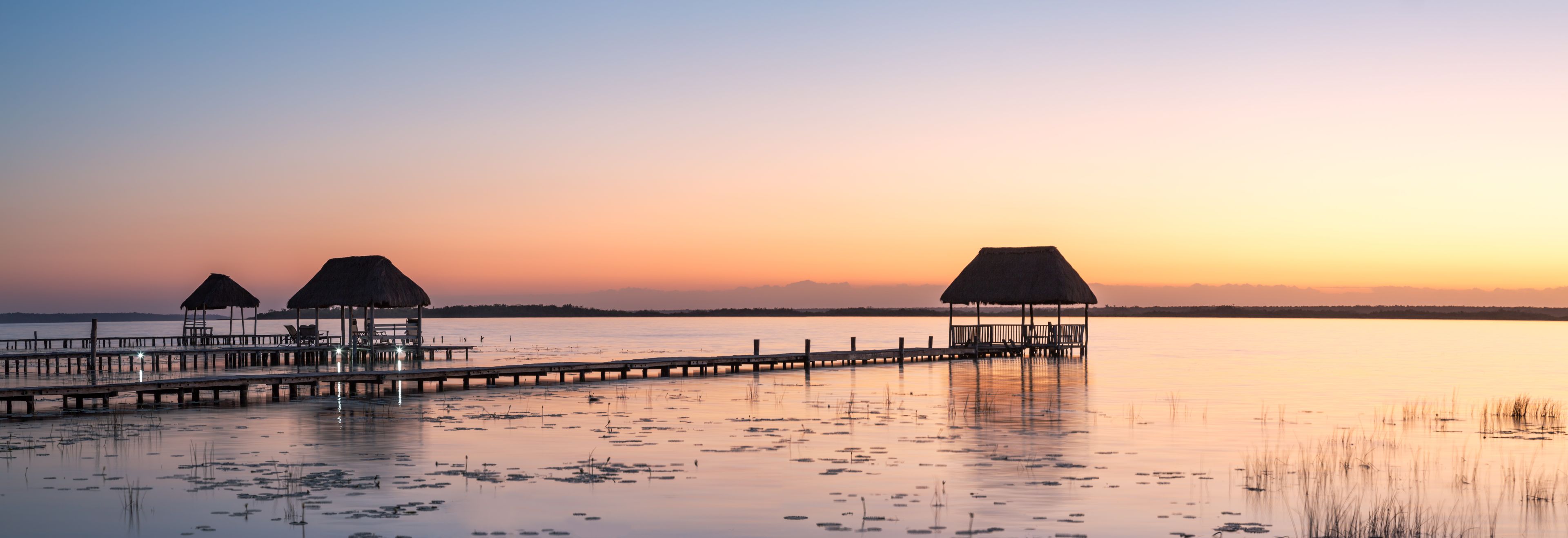 A pier extending into calm waters with thatched-roof structures at the end.