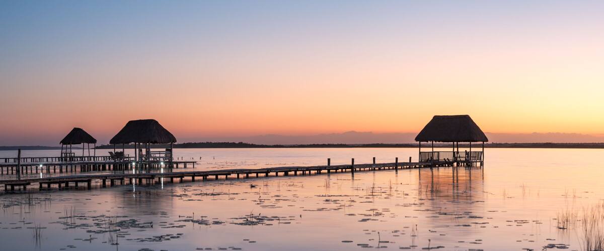 A pier extending into calm waters with thatched-roof structures at the end.