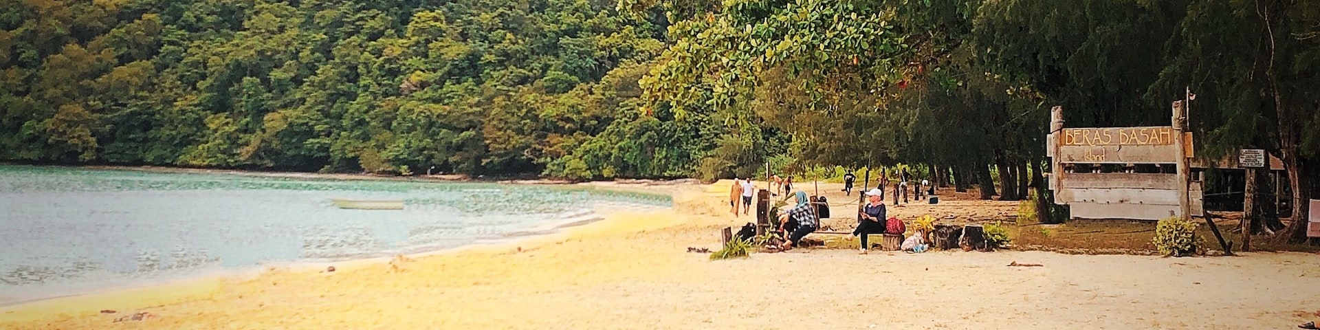 A beach with people relaxing, a sign reading "BERAS BASAH," and a dense forest in the background.