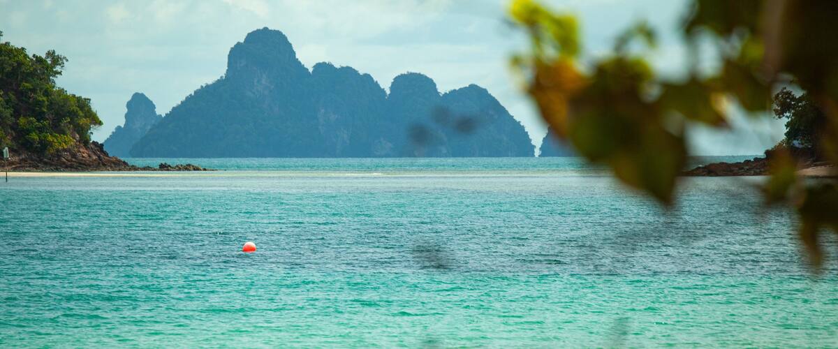 A turquoise sea with a buoy, a beach, and a mountain range in the distance.