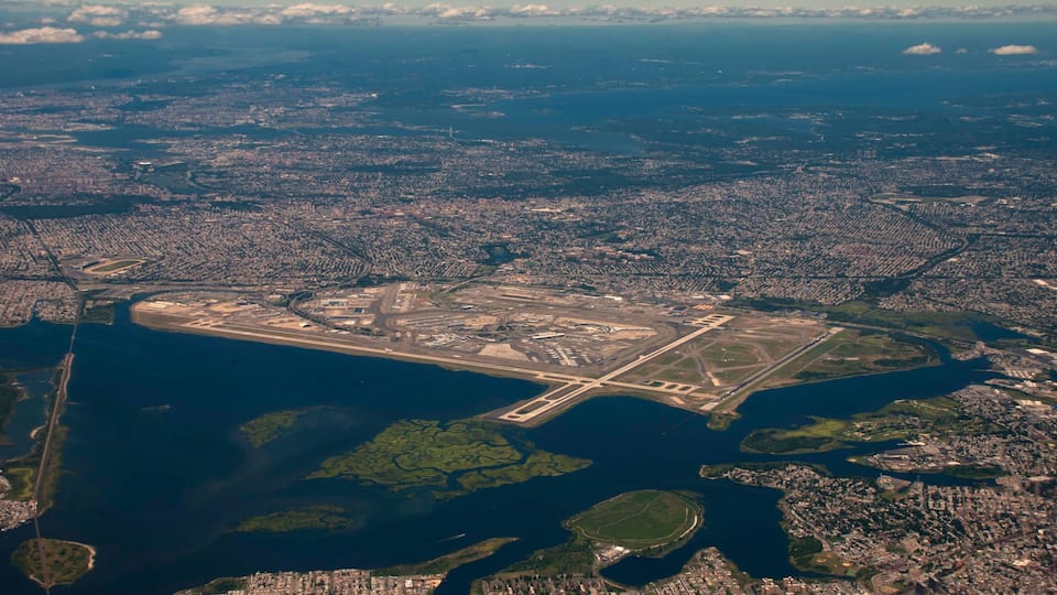 An aerial view of a coastal city with a large airport, dense urban areas, and a prominent body of water.