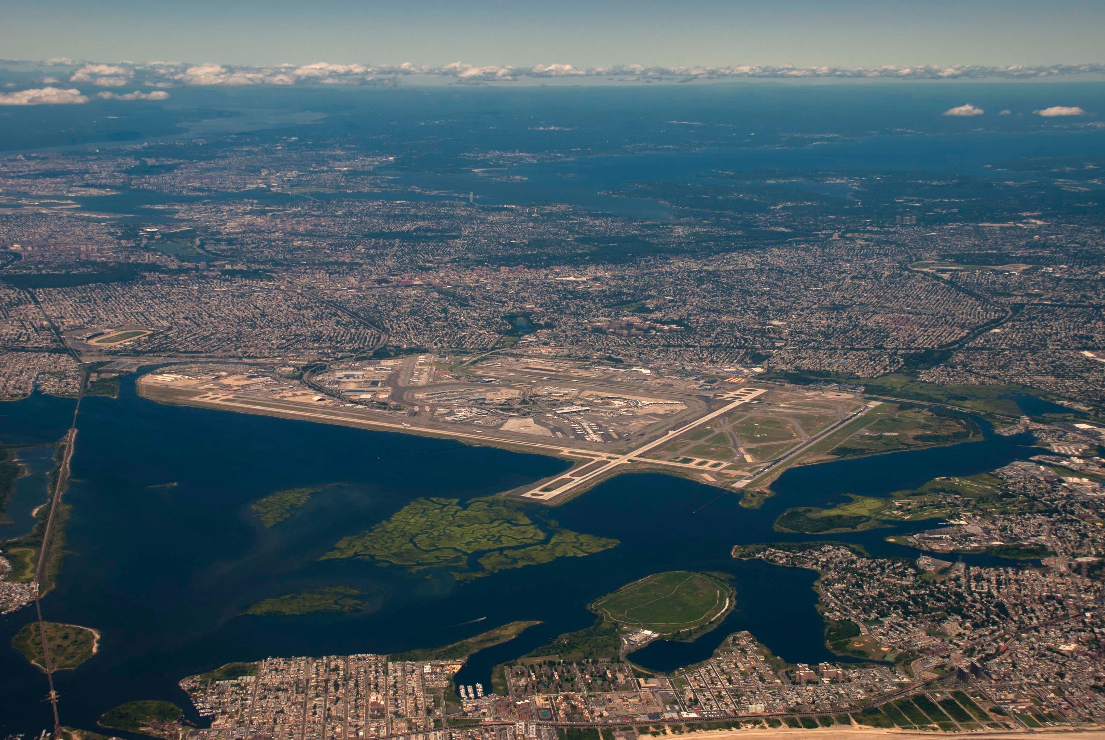 An aerial view of a coastal city with a large airport, dense urban areas, and a prominent body of water.