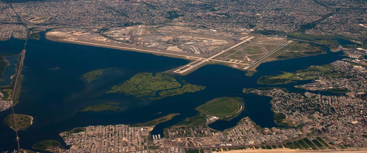 An aerial view of a coastal city with a large airport, dense urban areas, and a prominent body of water.
