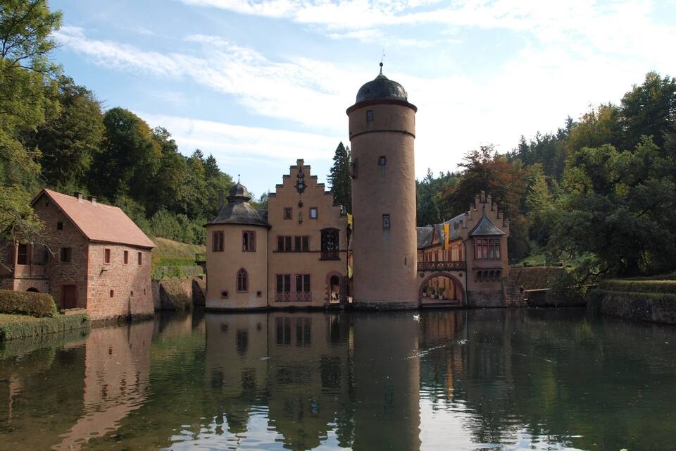 A castle with a tower by a calm lake surrounded by trees.