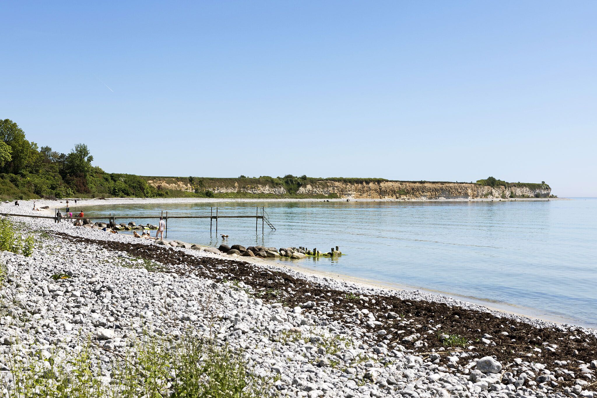 A rocky shoreline with a pier extending into calm waters, surrounded by cliffs and greenery.