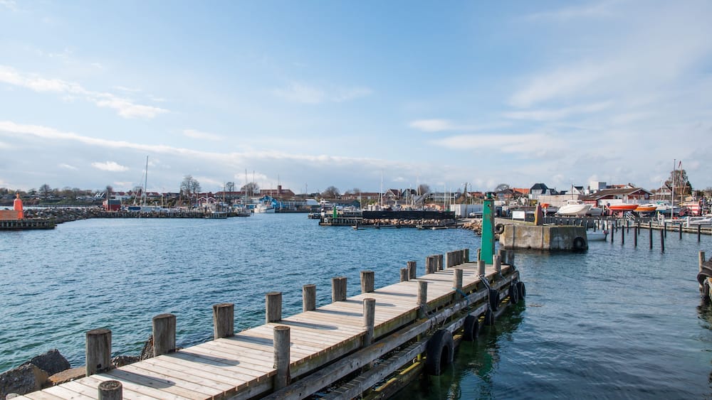 Une jetée en bois s’étendant sur une étendue d’eau calme, avec une ville et des bâtiments en arrière-plan.