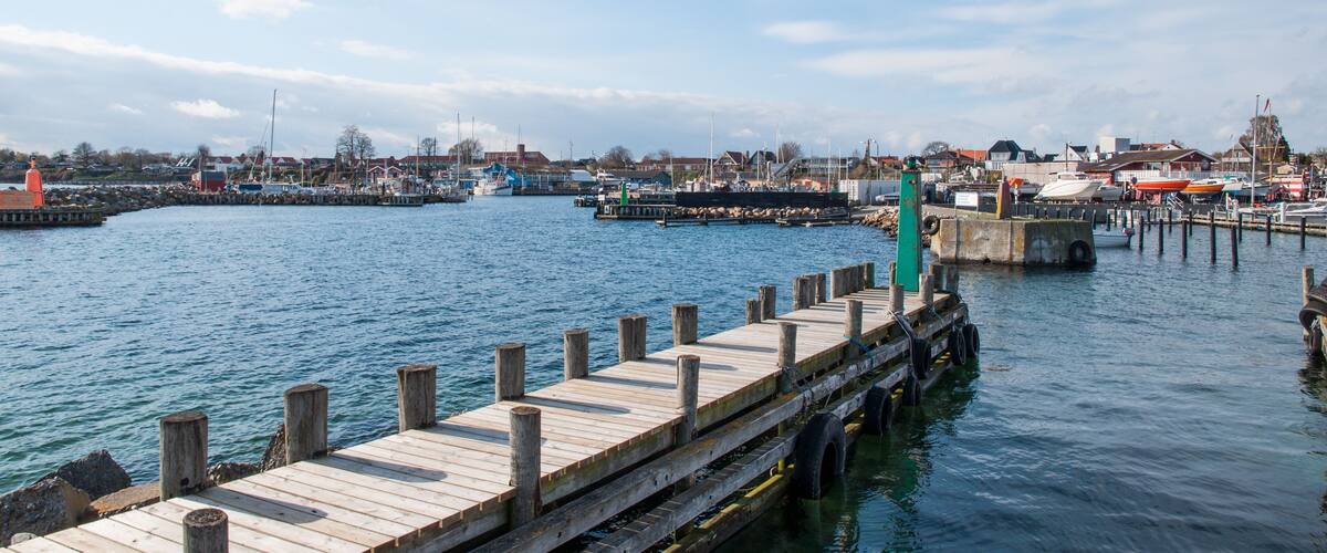 A wooden pier extending into calm water, with a town and buildings in the background.
