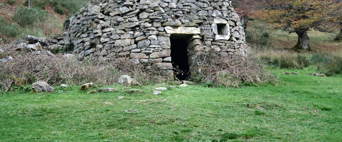 A stone hut with a small window, surrounded by grass and trees.