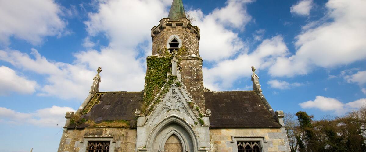 A historic stone church with a tall tower, arched entrance, and ivy-covered walls.