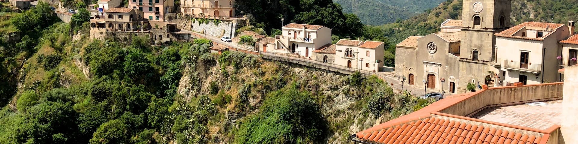 Savoca, one of the most beautiful villages in Italy, whose name is derived from the plant of the elder (savucu in Sicilian dialect), a shrub that still grows wild in the cracks between houses and which is represented in the medieval coat of arms of the village.
This small town set in the rock of a hill of dual tip, experienced the interest of kings, popes and Archimandrite prelates, in a succession of periods of serious crisis and prosperity. The basalt blocks lying on roads leading between separate small houses, freshly restored with Sicilian tiles on the roofs and windows framed in stone, then following streets in the rock here you’ll find extremely fragmented ruins and old cisterns.