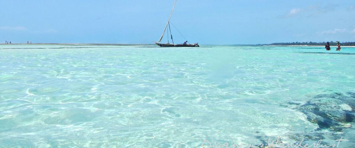 A clear blue sea with a sailboat anchored in shallow waters.