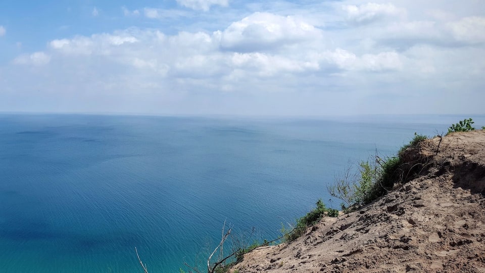 A coastal landscape with a clear blue sea, sandy cliffs, and sparse vegetation.