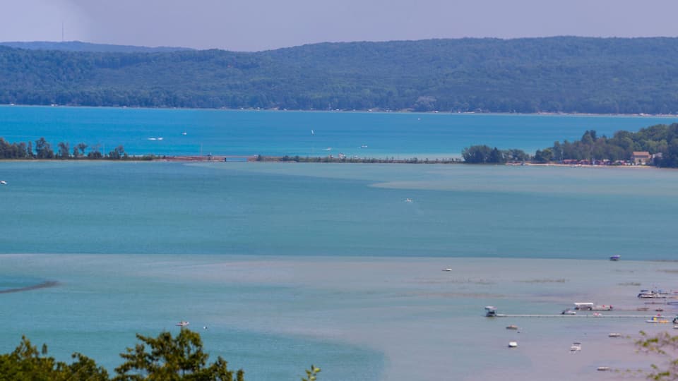 A coastal landscape with a clear blue sea, a sandy beach, and a forested hill in the background.