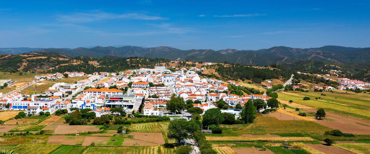 A town with white and orange buildings surrounded by green fields and mountains.