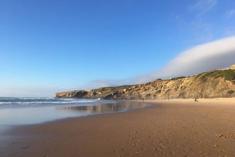 Een zandstrand met voetafdrukken, een rotsklif en de oceaan.