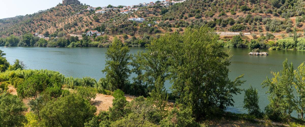 A lake surrounded by hills with a castle on a hilltop and houses scattered across the landscape.