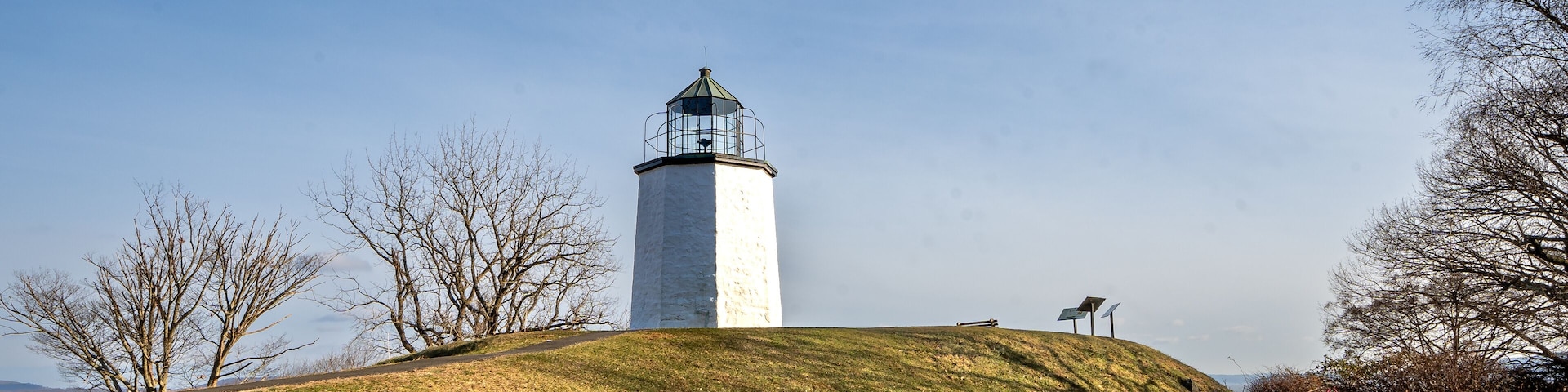 A lighthouse on a grassy hill with bare trees and rocks.