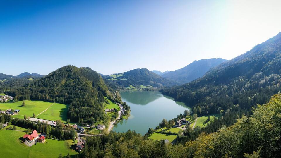 A lake surrounded by mountains, a village with houses, and green fields.