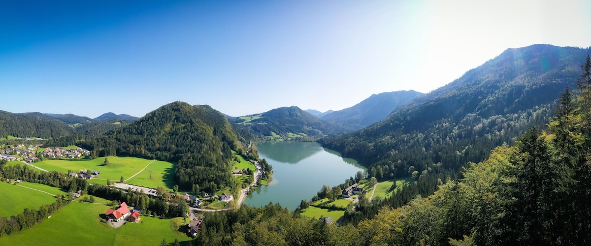 A lake surrounded by mountains, a village with houses, and green fields.