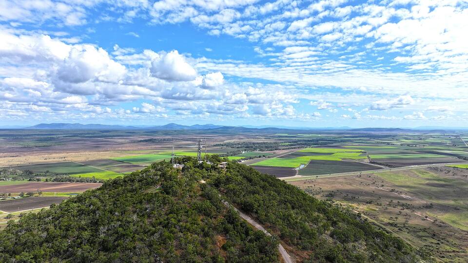 A mountainous landscape with a clear sky, green fields, and distant mountains.