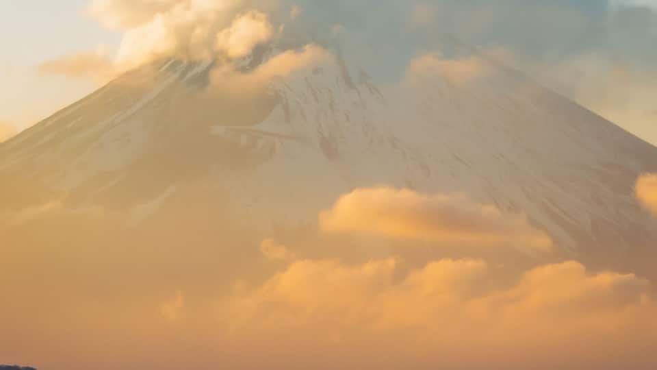 Aerial view of Mount Fuji's snow-capped peak piercing through golden clouds at sunset, a majestic sight from afar, Mt. Taikan Observation Deck, Kanagawa, Japan.