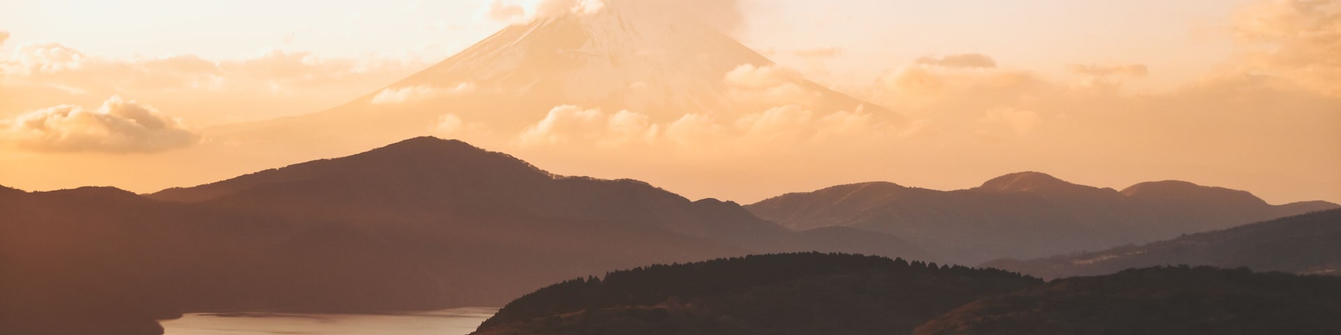View of the majestic Mount Fuji rising through the clouds, a serene lake reflecting the soft golden light of dusk, Mt. Taikan Observation Deck, Yugawara, Kanagawa, Japan.