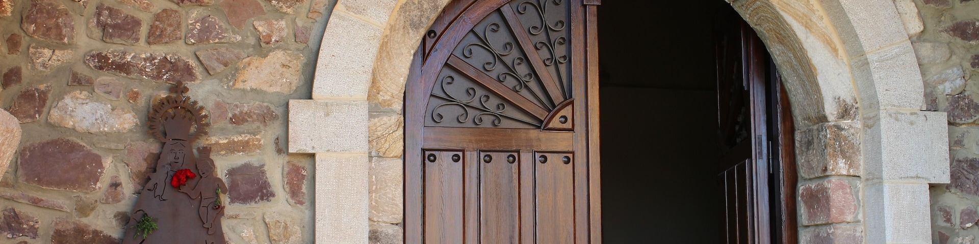 A stone wall with a wooden door and a sign that reads "Ermitas de Nuestra Sra de Olmecada."