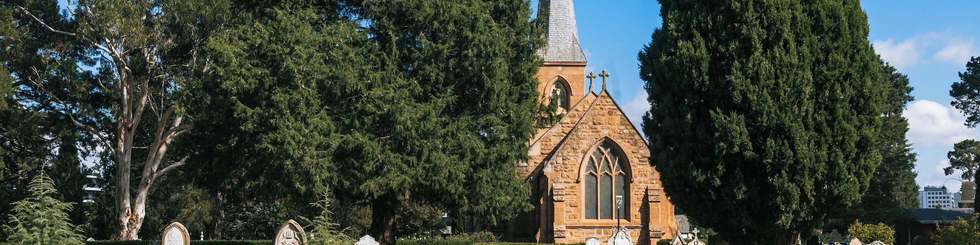 Eine Kirche mit einem hohen Turm, umgeben von Bäumen und einem Friedhof mit Grabsteinen.