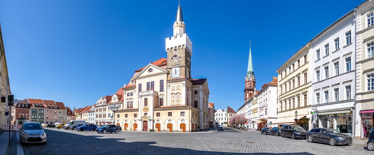 A historic square with a prominent church featuring a tall tower and a spire, surrounded by classic European architecture and cobblestone streets.
